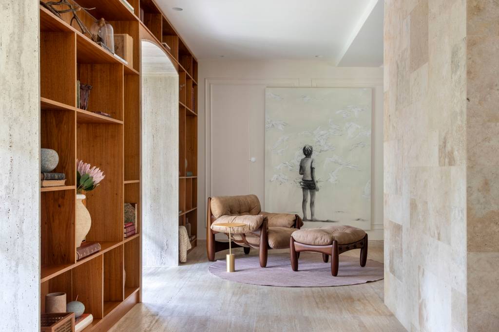 Casa em estilo clássico europeu tem piso mármore e árvore na área gourmet. Projeto de Studio LAK. Na foto, estante, poltrona mole com pufe.