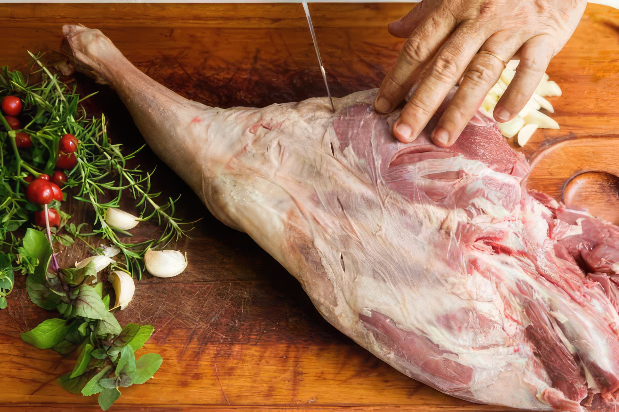 Imagem que mostra um pernil de cordeiro sendo assado na churrasqueira, com o churrasqueiro acompanhando o processo de preparo. A carne apresenta um dourado suculento e apetite, cercada por um ambiente t&iacute;pico de festas ao ar livre.
