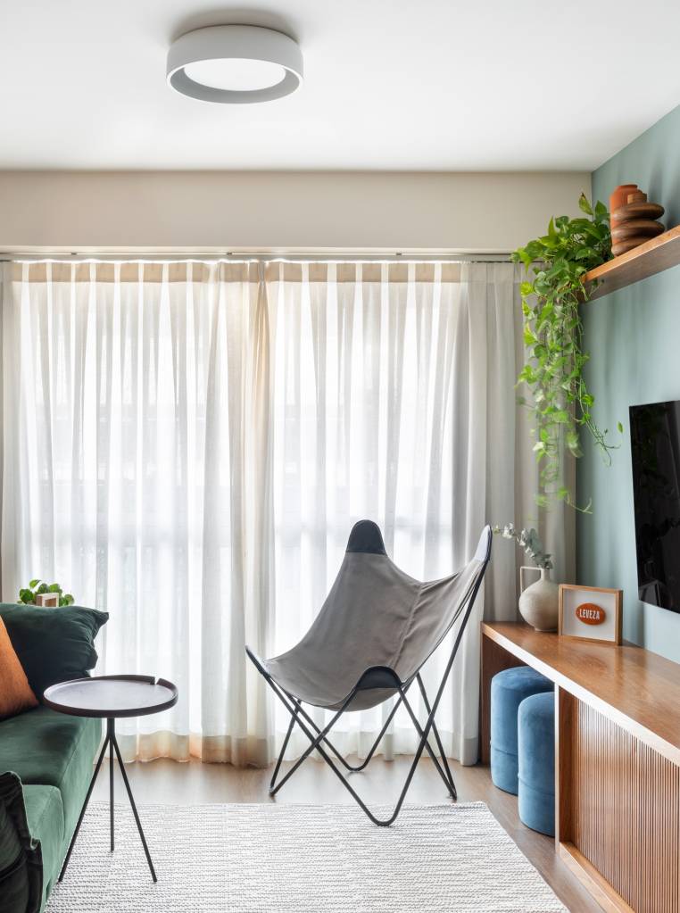 Renovação econômica deixa apê de 70 m² mais colorido com laranja e verde. Projeto Co+Lab Juntos Arquitetura. Na foto, sala de estar, poltrona, cortina, planta suspensa.