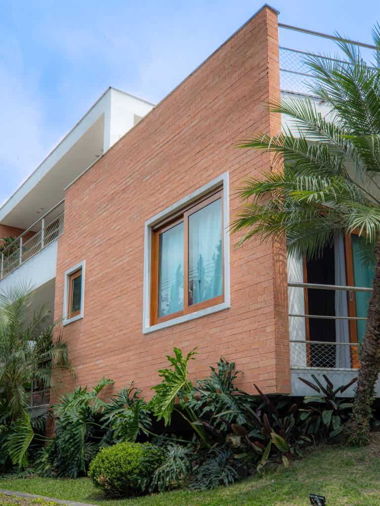 Casa em Teresópolis tem esquadrias, tijolinhos e cimento queimado na fachada. Projeto de Viviane Cunha.