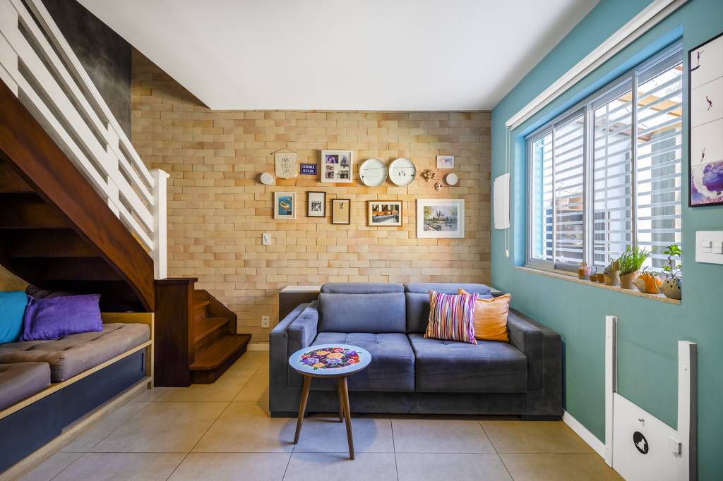 Charmoso sobrado azul tem projeto guiado pelo Feng Shui e solário. Projeto de BTliê Arquitetura. Na foto, sala, parede de tijolinhos, sofá azul.