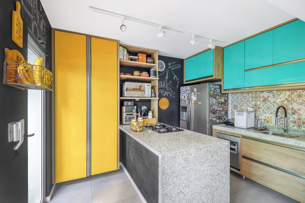 Charmoso sobrado azul tem projeto guiado pelo Feng Shui e solário. Projeto de BTliê Arquitetura. Na foto, cozinha, armário amarelo.