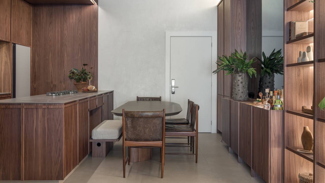Estilo contemporâneo e design assinado são destaque em apartamento de 105 m². Projeto de Renata Niero. Na foto: sala de jantar integrada à cozinha, ilha, marcenaria, nogueira