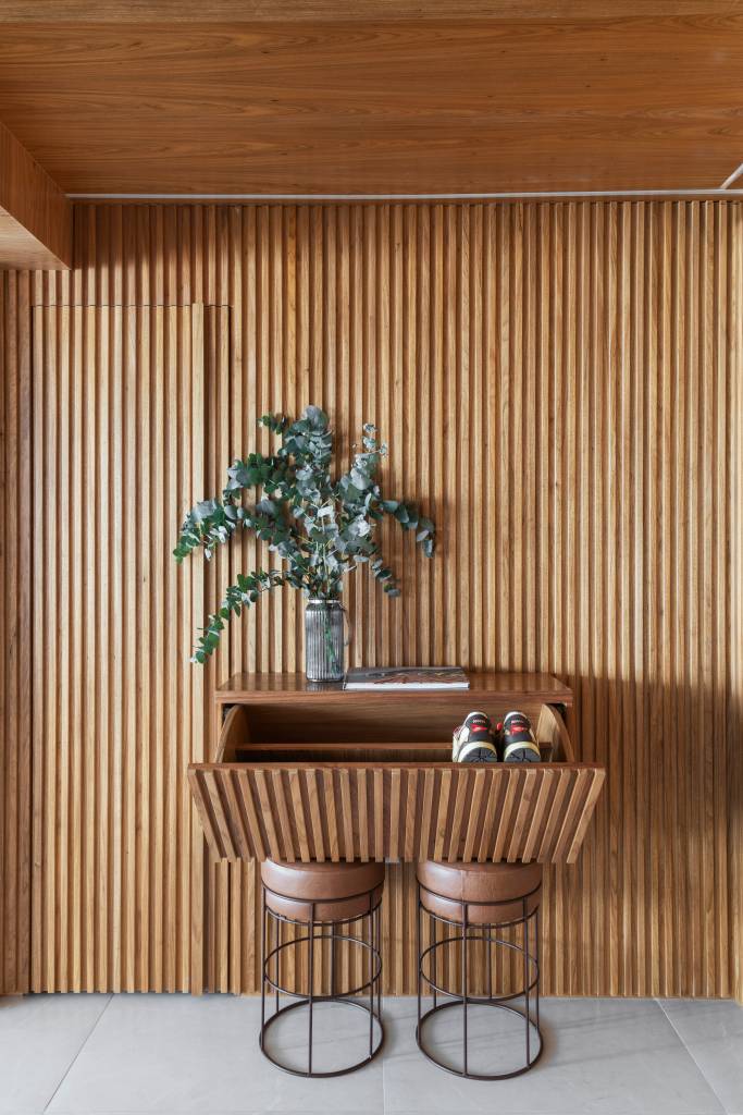 Apê tem adega de madeira escura em parede revestida com pedras brancas. Projeto de Daniela Coli.