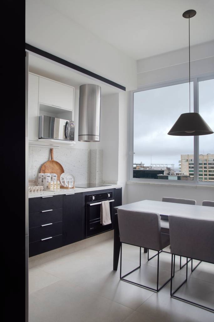 Apê tem quarto integrado à sala com porta articulada e cozinha preta e branca. Projeto de RIcardo Melo e Rodrigo Passos.