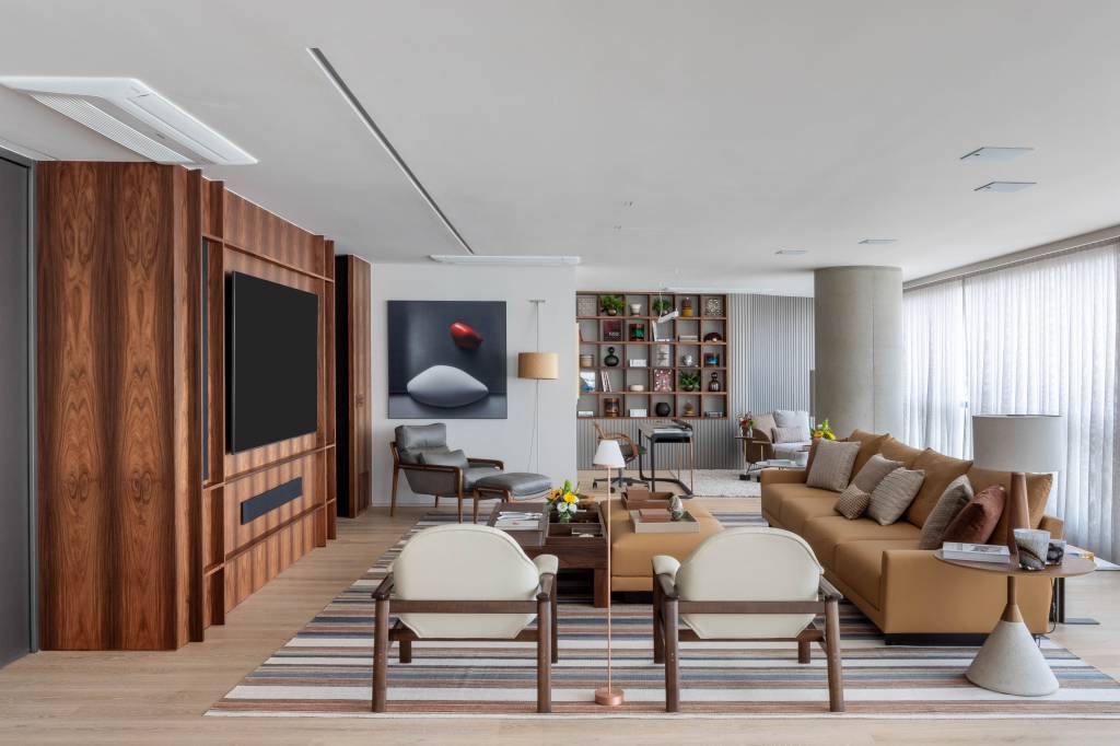 Painel em marcenaria curvo envolve sala e abriga estante com nichos neste apê