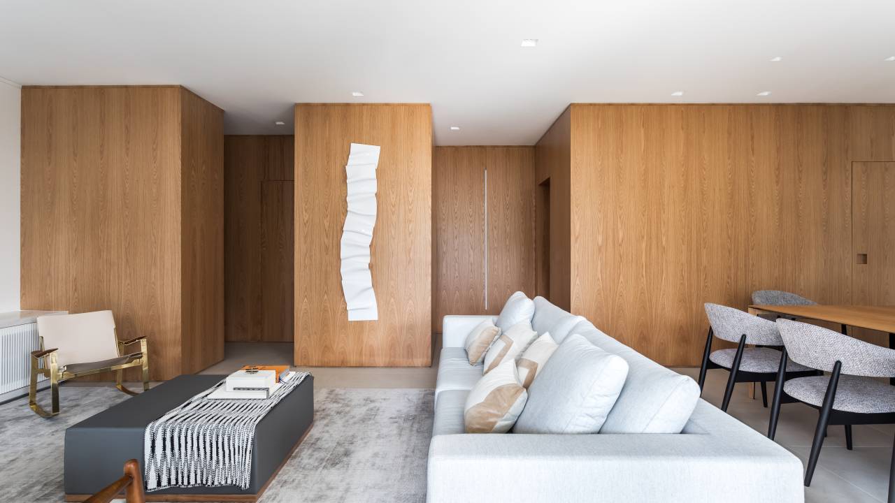 Painéis em lâmina natural de carvalho americano revestem paredes de apartamento. Projeto de ARQ+CO Studio.