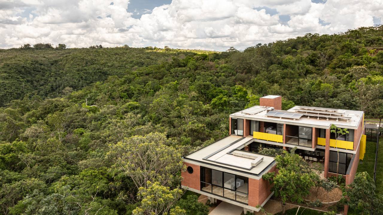 Passarela com brises metálicos amarelos conectam áreas desta casa no mato. Projeto de Hersen Mendes Arquitetura.
