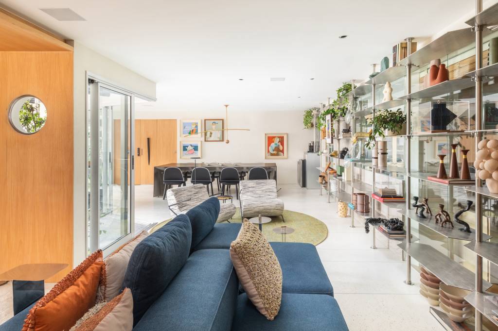 Estante em aço inox é peça que cria continuidade em área social de apê integrado