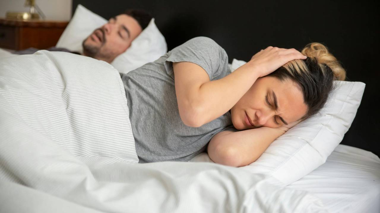 Mulher tentando dormir, mas não conseguindo por causa do barulho.