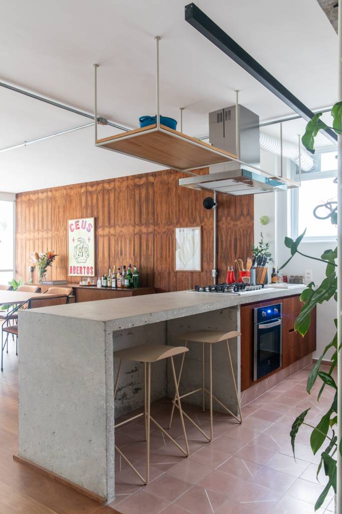 Neste apê, estante metálica branca é divisória e floreira para jiboias e costelas-de-adão. Projeto de Península Arquitetura.