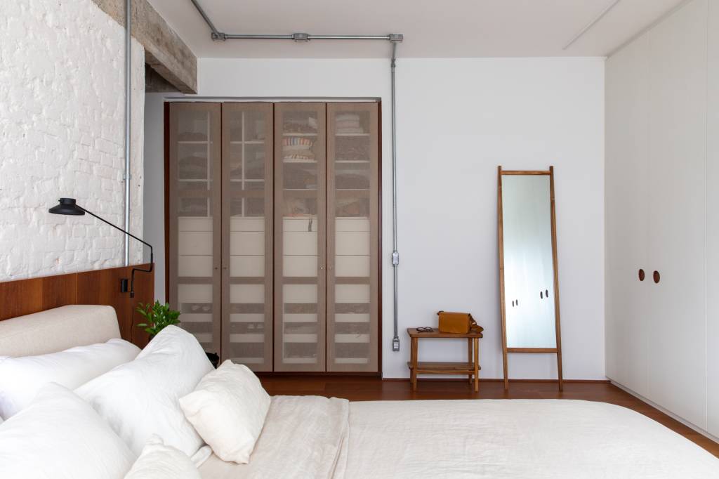 Neste apê, estante metálica branca é divisória e floreira para jiboias e costelas-de-adão. Projeto de Península Arquitetura.