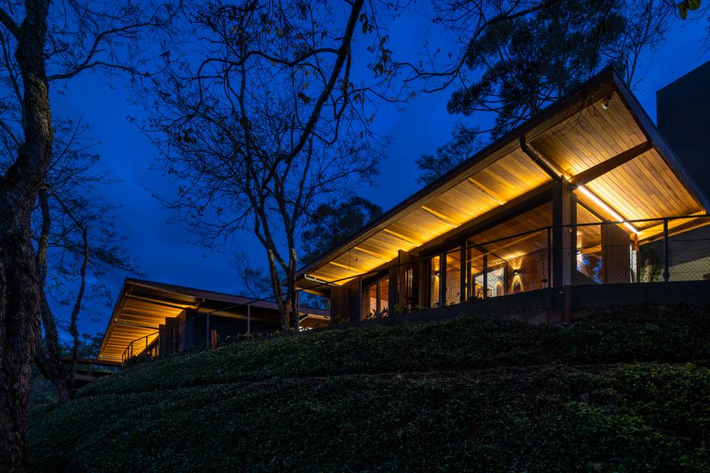Com uso da madeira e integração com a natureza, casa térrea de 250 m² vira refúgio no interior de SP, Projeto de Sabella Arquitetura. Fachada iluminada à noite.