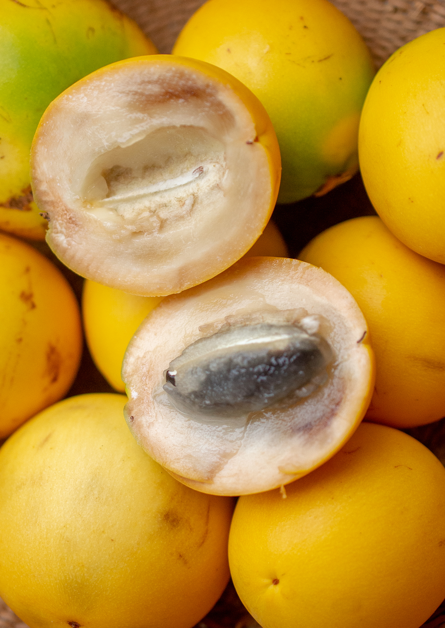 Frutas amarelas de bacupari, duas cortadas ao meio revelando polpa clara e sementes escuras, sobre outras frutas inteiras